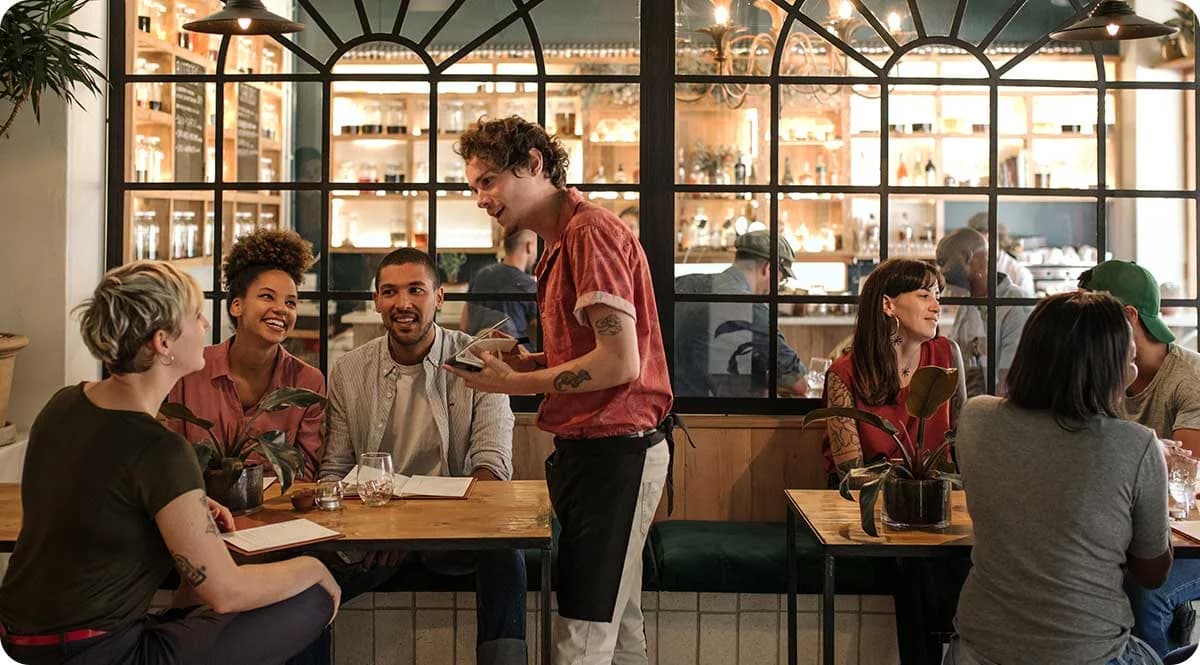 Kellner im Gespräch mit einer Gästegruppe an einem Restauranttisch