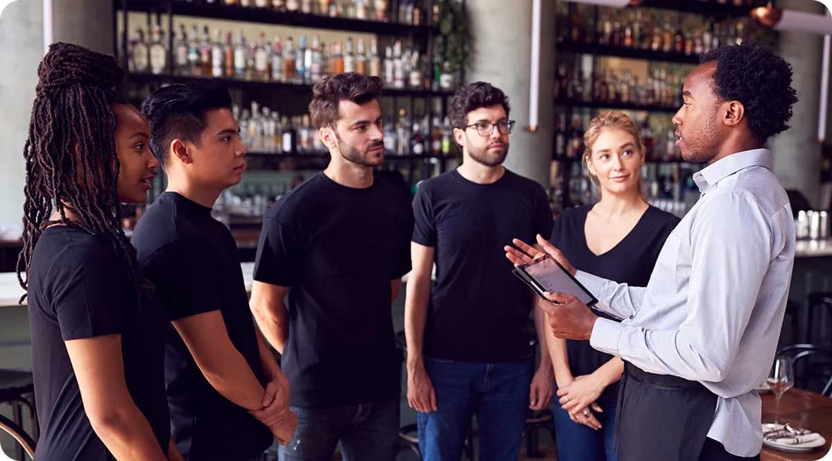 Restaurantleiter bespricht mit seinem Team Rückmeldungen auf einem Tablet